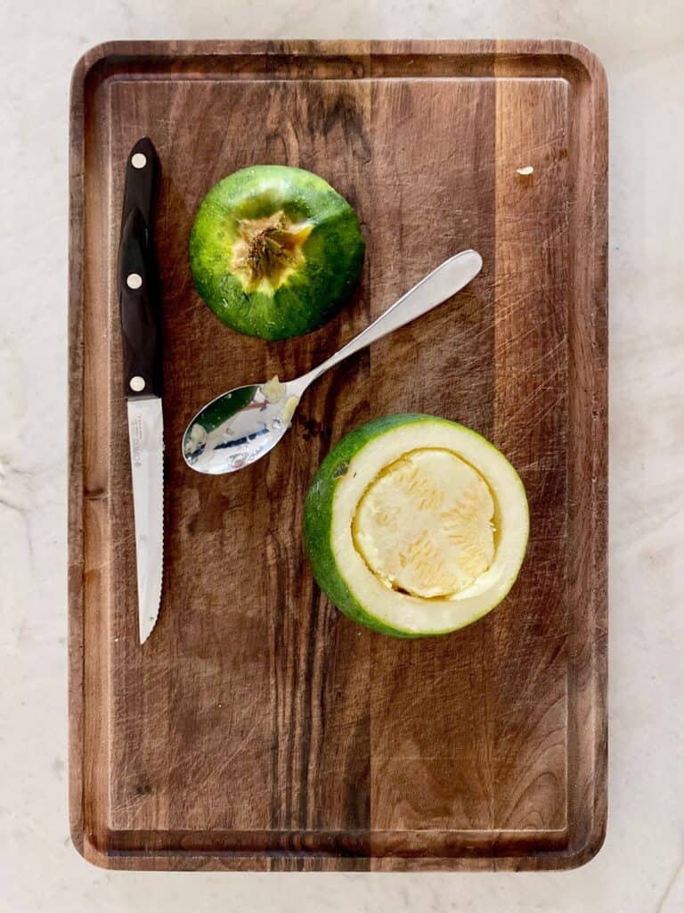 top view od 8 ball zucchini on wood board partially scooped next to spoon and knife